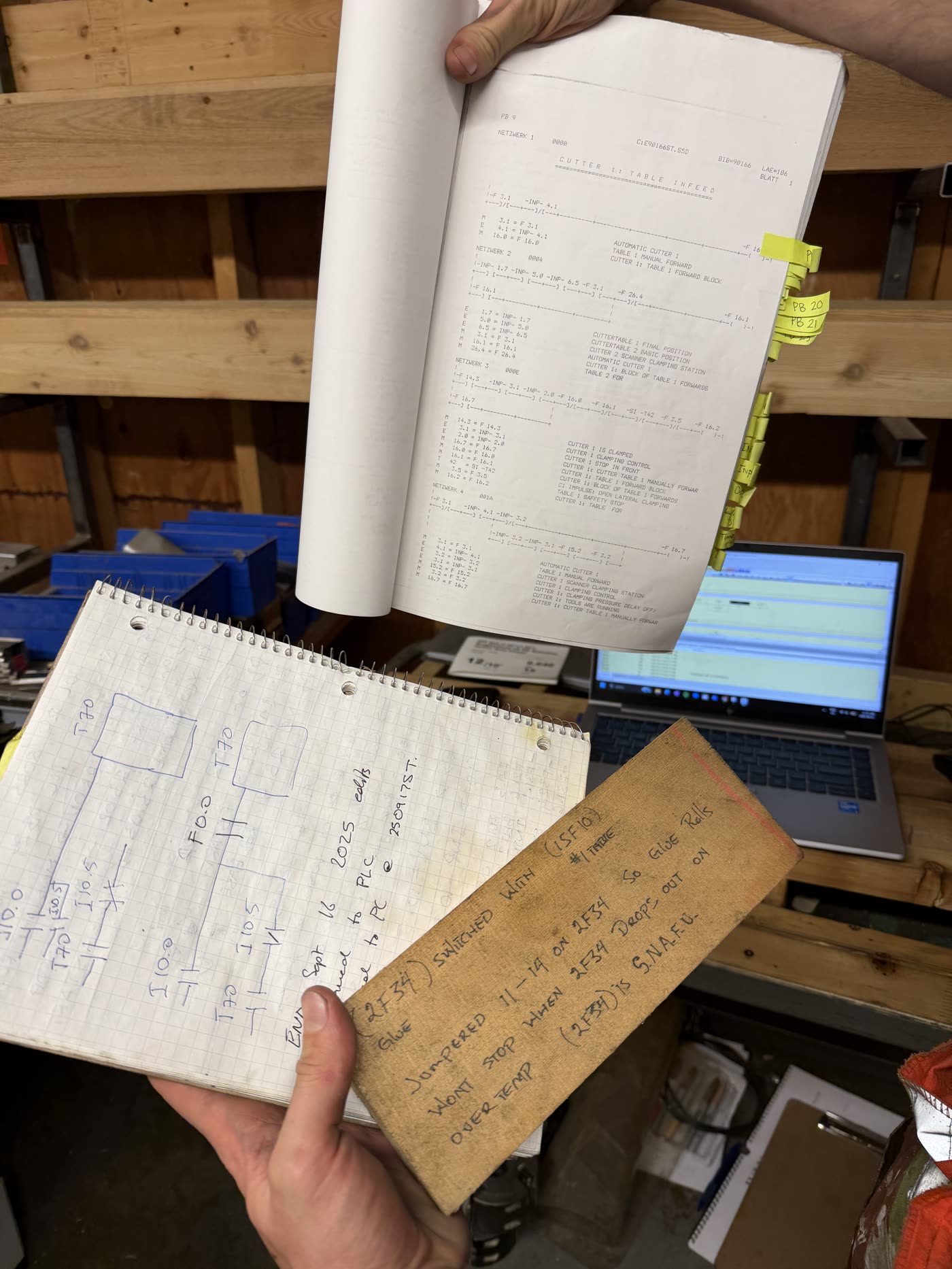 The tabbed ladder printout, a notebook of hand-drawn rungs, and a wooden board of wiring notes