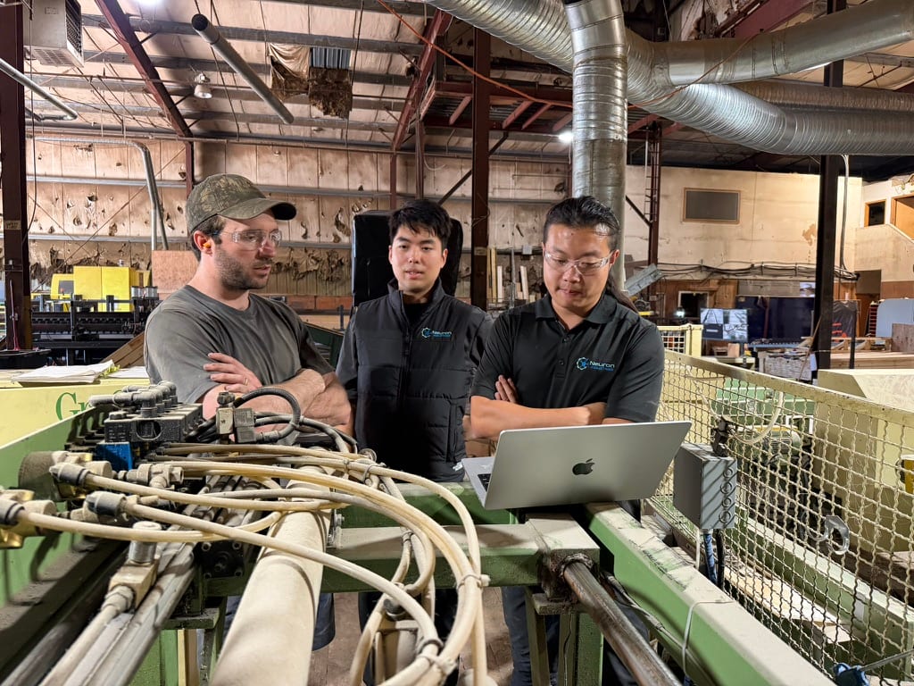 Three engineers reviewing a laptop beside the production machinery at CureWood.