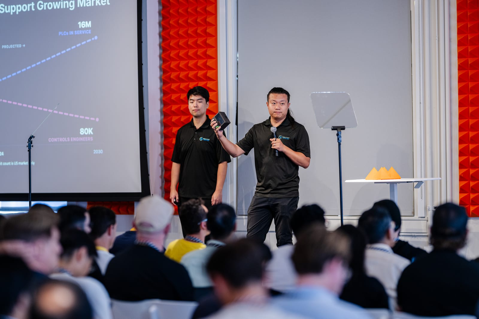 The Neuron founders on stage at YC Demo Day, presenting an industrial controller to the audience.