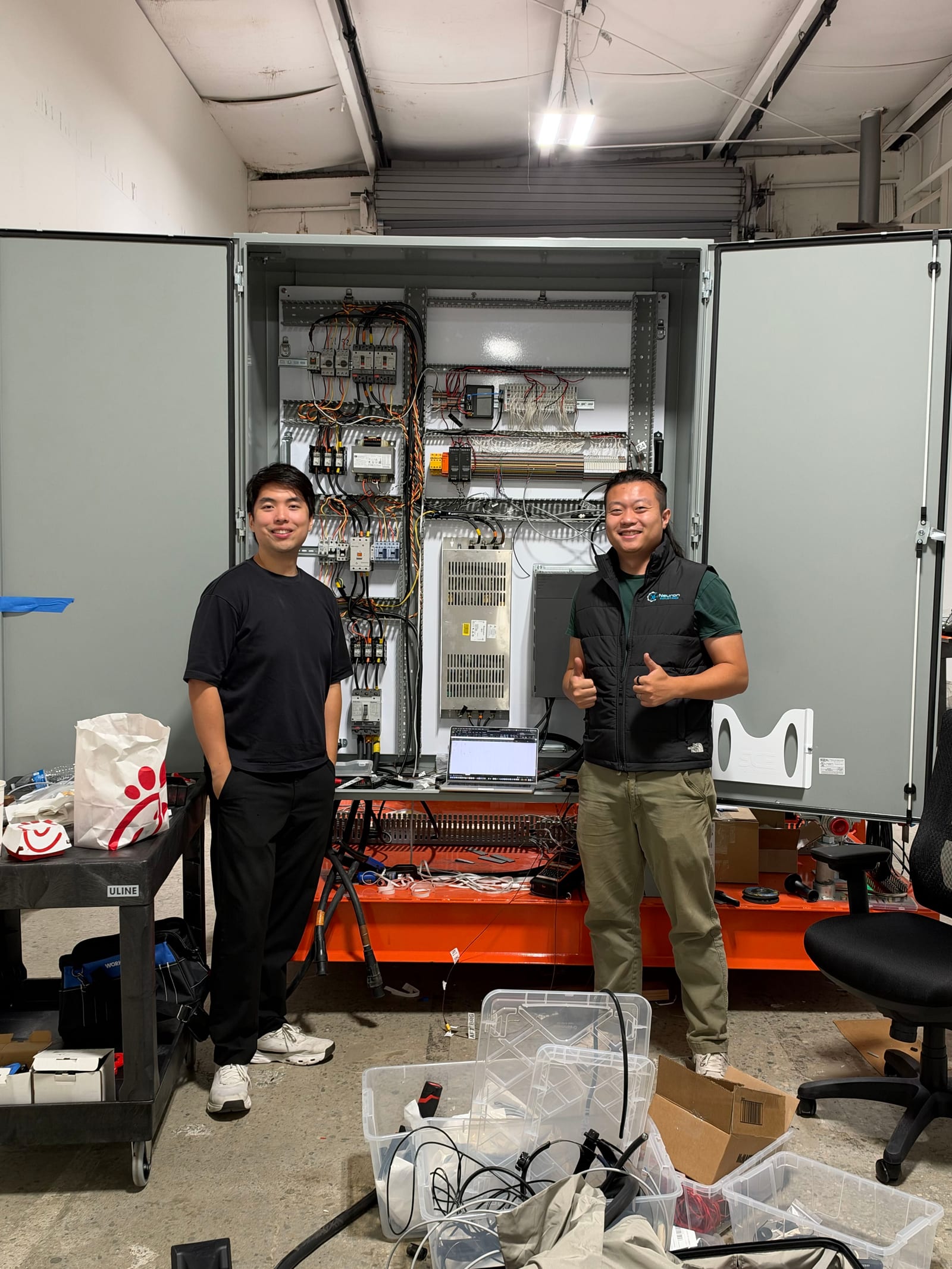 The Neuron founders standing beside an open industrial control cabinet at Lazarus Energy.